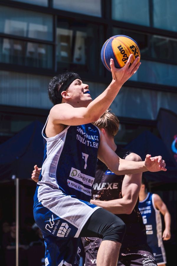 屋外の3x3の試合で、ディフェンスをかわしてレイアップシュートを打つ選手
